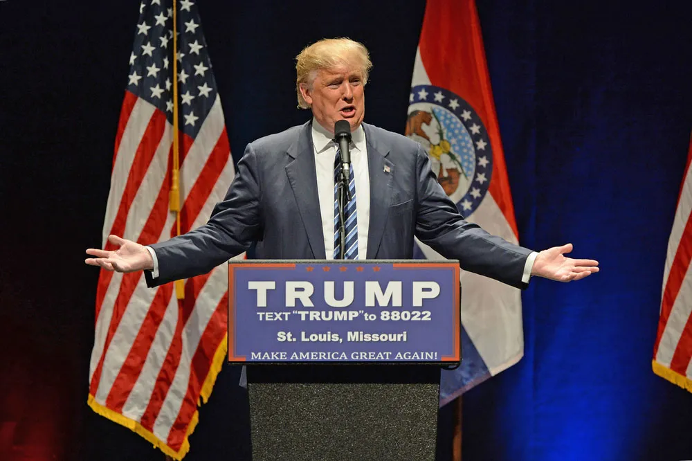 Donald Trump giving a speech at a podium, gesturing with his hand.