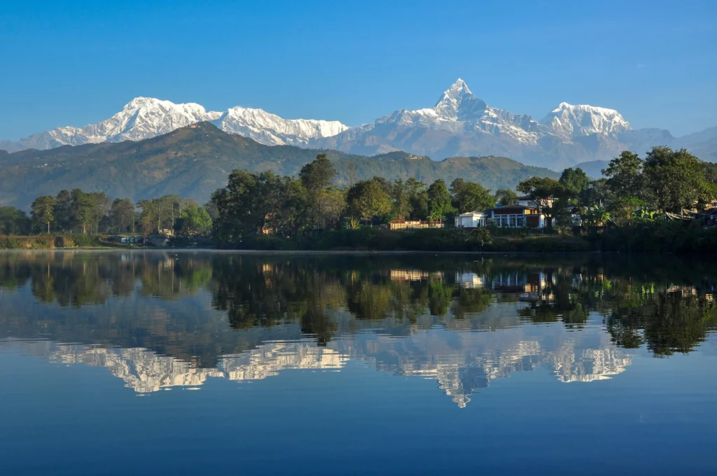 Stunning view of Phewa Lake in Pokhara with colorful boats floating on the calm water and the Annapurna mountains reflected in the lake.