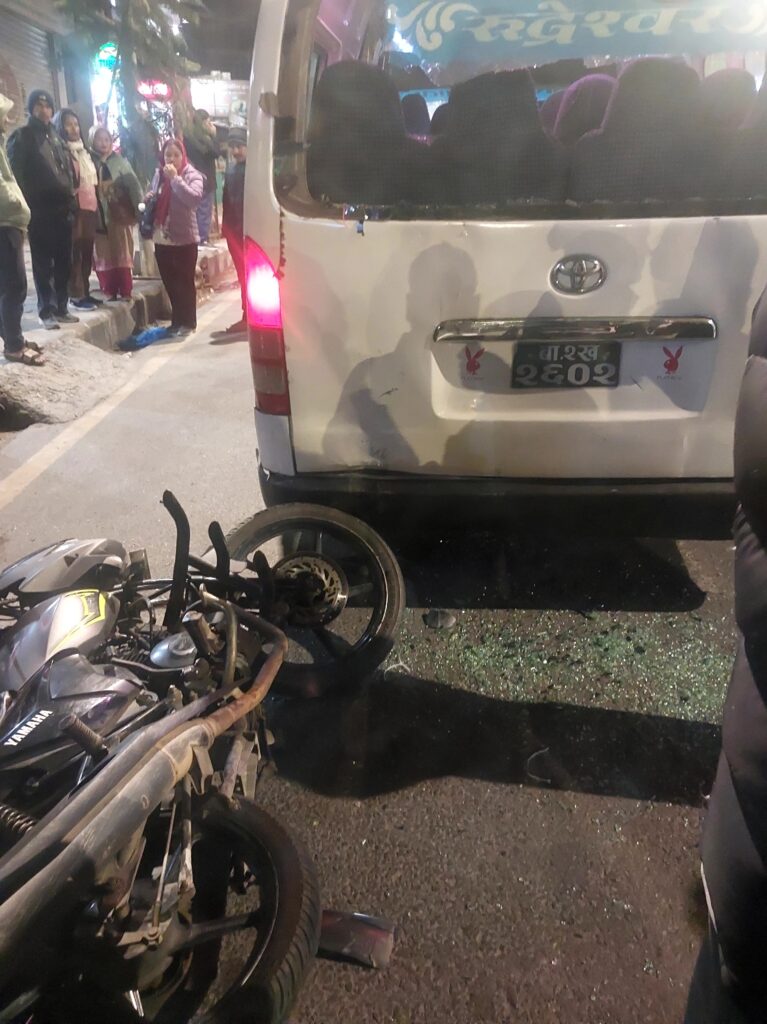 Microbus and motorcycle accident at Deuwa Chowk in Budhanilkantha during the evening, with the bike lying on the road and people gathered around helping the injured.